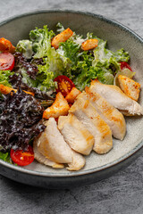 Healthy chicken salad with grilled breast fillet, fresh lettuce, cherry tomatoes, croutons, and creamy dressing served in a ceramic bowl on gray background