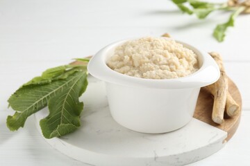 Tasty horseradish sauce and roots on white wooden table, closeup
