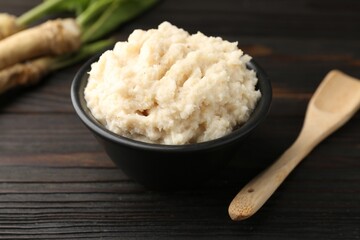 Tasty horseradish sauce and roots on black wooden table, closeup