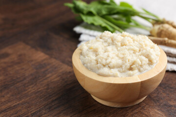 Tasty horseradish sauce and roots on wooden table, closeup. Space for text