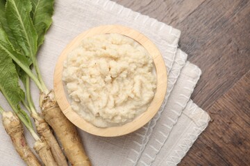Tasty horseradish sauce and roots on wooden table, flat lay