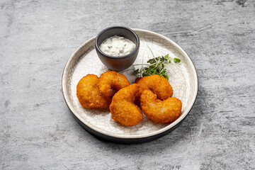 Crispy golden fried shrimp served with creamy tartar sauce and fresh microgreens on a round white ceramic plate with cracked pattern on gray stone background
