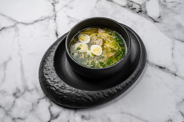 Traditional chicken noodle soup with boiled egg slices, fresh dill, and vegetables served in a black ceramic bowl on marble table
