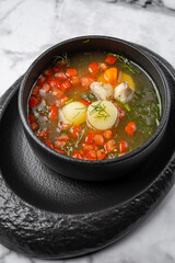 Traditional fish soup with potatoes, carrots, red pepper, and herbs served in a black ceramic bowl on marble table