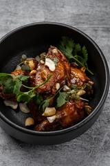 Glazed chicken wings with cashew nuts and fresh cilantro served in a black ceramic bowl on gray rustic background