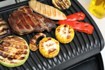 Electric grill with tasty meat and vegetables on table, closeup