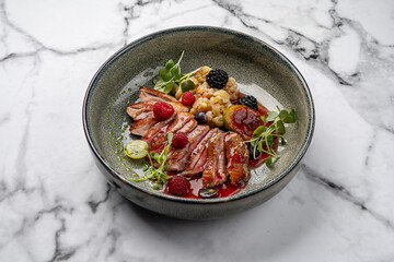 Gourmet duck breast fillet with berry sauce, fresh raspberries, blackberries, figs, grapes, cauliflower and microgreens served on ceramic plate with marble background