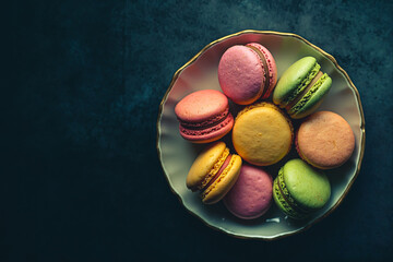 Multicolored French macarons in a plate against a black vintage background. Top view.