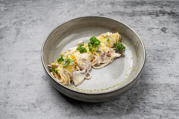 Spaghetti pasta with creamy white sauce, grated cheese, fresh herbs and ham served in ceramic bowl on gray stone background, close up