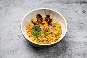 Seafood risotto with mussels, shrimp, parmesan cheese and fresh herbs served in a ceramic bowl on gray stone background, traditional Italian cuisine