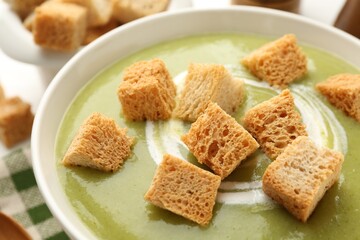 Tasty broccoli cream soup with croutons in bowl on table, closeup