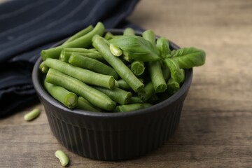 Pieces of fresh green beans and basil leaves in bowl on wooden table, closeup