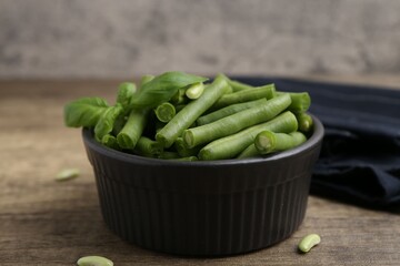 Pieces of fresh green beans and basil leaves in bowl on wooden table, closeup