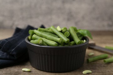 Pieces of fresh green beans in bowl on wooden table, closeup