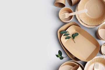 Set of disposable tableware and green leaves on white background, flat lay. Space for text