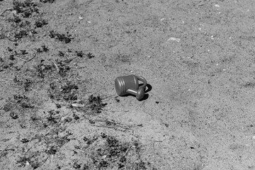 A lonely, small watering can lies abandoned on the ground, creating a poignant and minimalist black and white composition. The image evokes a sense of nostalgia and quiet solitude.

