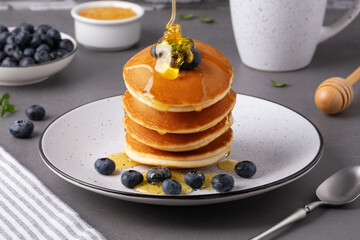 A stack of pancakes is drizzled with honey. Blueberries are placed next to the pancakes