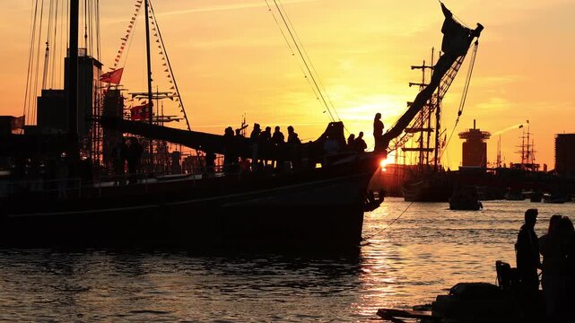 silhouette of tall ships cruising on golden IJ river against sunset during Sail Amsterdam 2025, tall ships romantic