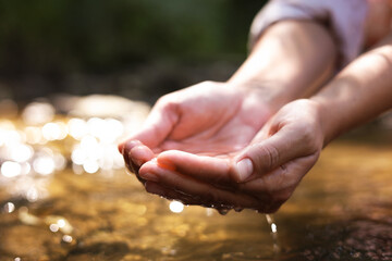 Save water concept. Woman holding clean water in her hands near river outdoors, closeup