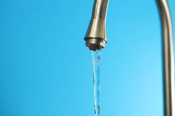 Water saving concept. Stream of water flowing from tap on light blue background, closeup. Space for text