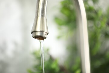 Water saving concept. Stream of water flowing from tap indoors, closeup. Space for text