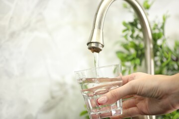 Water saving concept. Woman filling glass with tap water indoors, closeup. Space for text