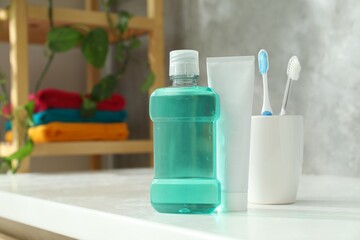 Bottle of mouthwash, toothbrushes and toothpaste on white table in bathroom. Space for text