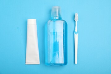Mouthwash, toothbrush and toothpaste on light blue background, flat lay