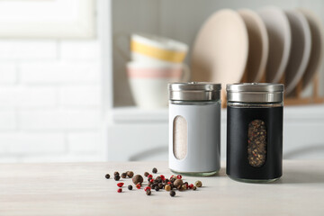 Salt, pepper shakers and peppercorns on light wooden table in kitchen, closeup. Space for text