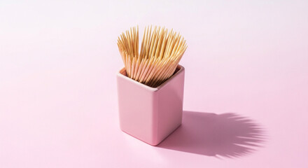 Photo of a pink ceramic holder filled with wooden toothpicks sits on a pink surface, casting a long shadow
