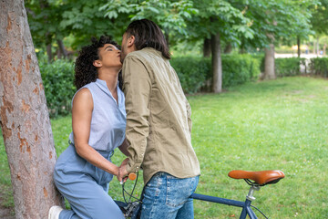 Interracial couple kissing in the park next to vintage bicycle