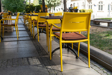 An empty street cafe or restaurant terrace with a loy of wooden tables and yellow chairs, no people.