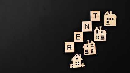 Naklejka premium real estate houses with rent word made with wooden blocks on black background. Mortgage commitments and rental flexibility concept