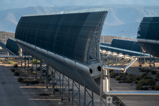 Solar thermal power station with rows of parabolic trough mirrors reflecting sunlight. Heatwave coming out from the pipe.