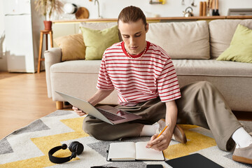 Young handsome man studies on a cozy living room floor with a laptop and notebook