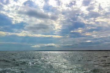 Obraz premium Sun rays shinning through the clouds over the ocean. Cloudy sky with sun rays coming down onto choppy ocean water