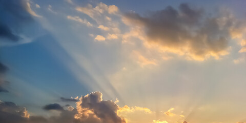 Sunset sky with blue, yellow and orange colors. Sun rays shinning through clouds in an upward direction. Colorful sunset sky with sunbeam wallpaper background