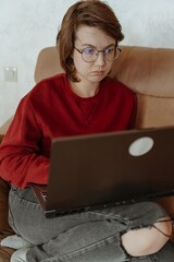 A young woman works on her laptop in a cozy living room, capturing the modern freelance lifestyle. Authentic moment of remote work, focus, and digital independence