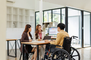 An inclusive modern office environment with a diverse team collaborating. A person in a wheelchair actively engages with colleagues.
