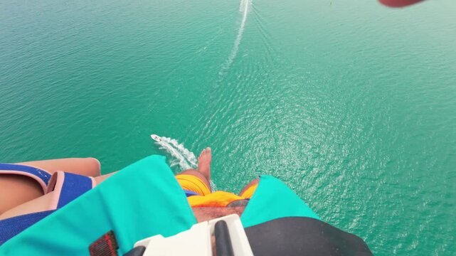 First Person parasailing. Legs above the seawater while parasailing. A boat pulling a parasailing couple while a speed boat passes under them