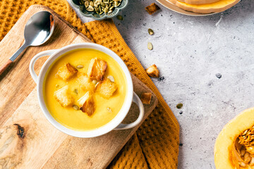 Bowl of pumpkin soup with croutons, seeds on concrete background