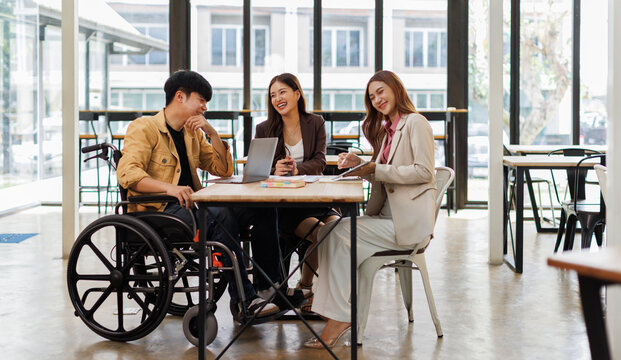 Asian Male Manager On A Wheelchair Sitting With His Colleagues At Workplace
