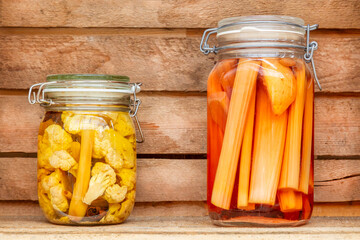 Two glass canning jars with preserved vegetables in front of a wooden wall