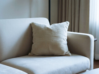 A light-colored sofa with a single cushion placed against a neutral background, featuring soft lighting and minimalistic decor.