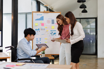 Happy business man on wheelchair and her female colleague cooperating while working on paperwork in the office.
