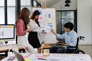 Happy business man on wheelchair and her female colleague cooperating while working on paperwork in the office.
