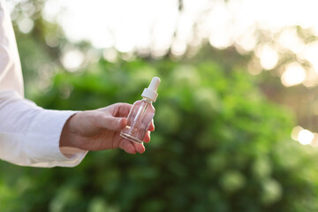 Cosmetic serum clear glass bottle in woman's hand outdoor at sunset. Natural beauty concept