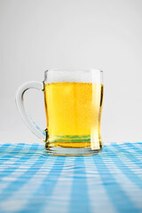 Beer mug with a blue checkered tablecloth or napkin on a white table. Concept of Oktoberfest. Bavarian German culture festival decoration symbol