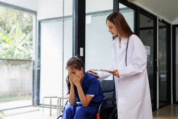 Obraz premium friendly female nurse staff caregiver of nursing home talking to asian young woman a wheelchair in hallway 