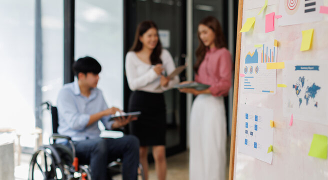 Group shot of diverse business people, disabled asian man on wheelchair chatting with colleagues together at meeting room at office
